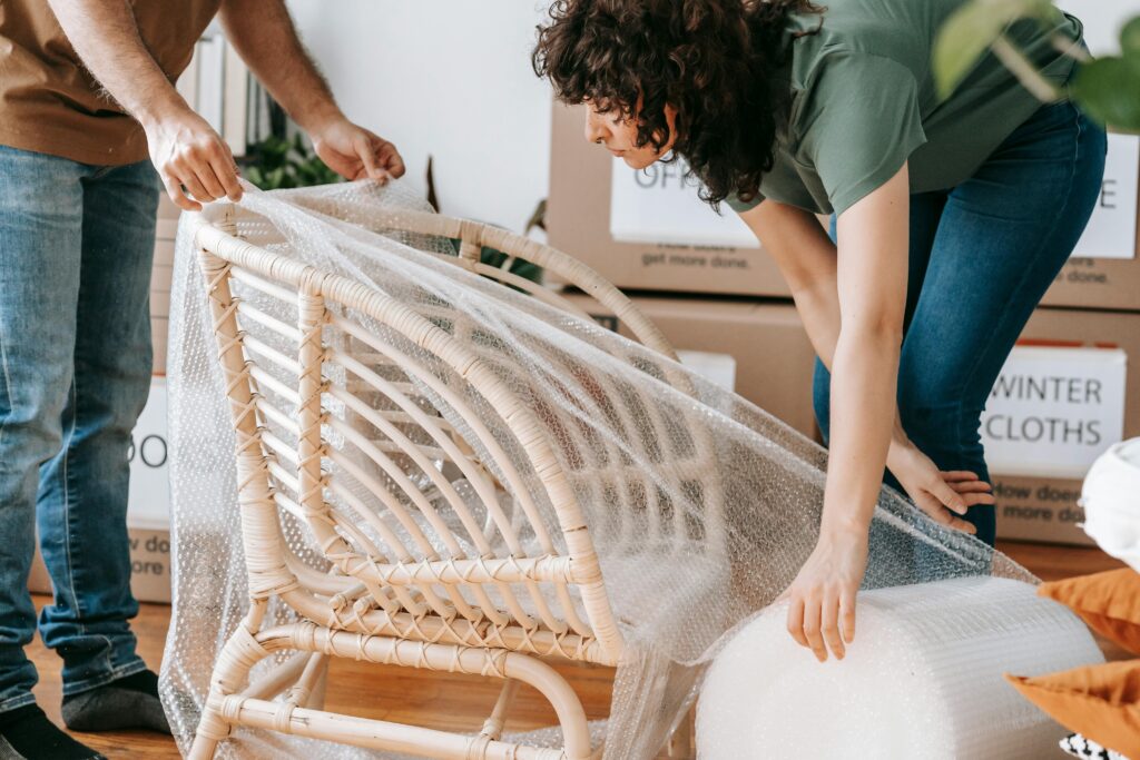 A couple uses bubble wrap to protect a chair while packing up their home for relocation.